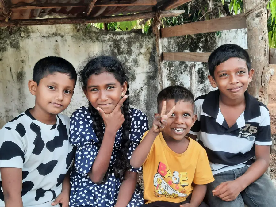 Vier kinderen uit Thariyankulama zitten lachend naast elkaar